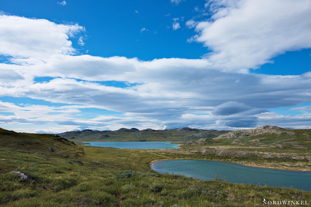 Blick über zwei blaue Seen unter blauem Himmel mit losen Wolken auf dem Arctic Circle Trail
