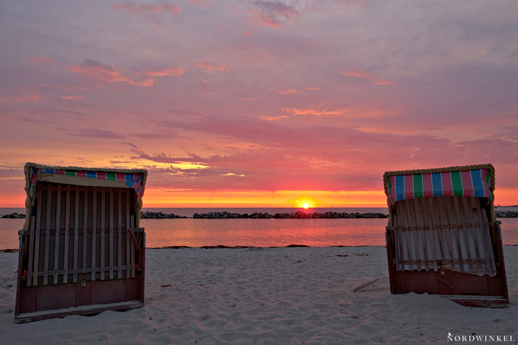 beach chairs at sunrise in the sand, baltic sea in the background and lightning sky with rising sun in shades of red and yellow
