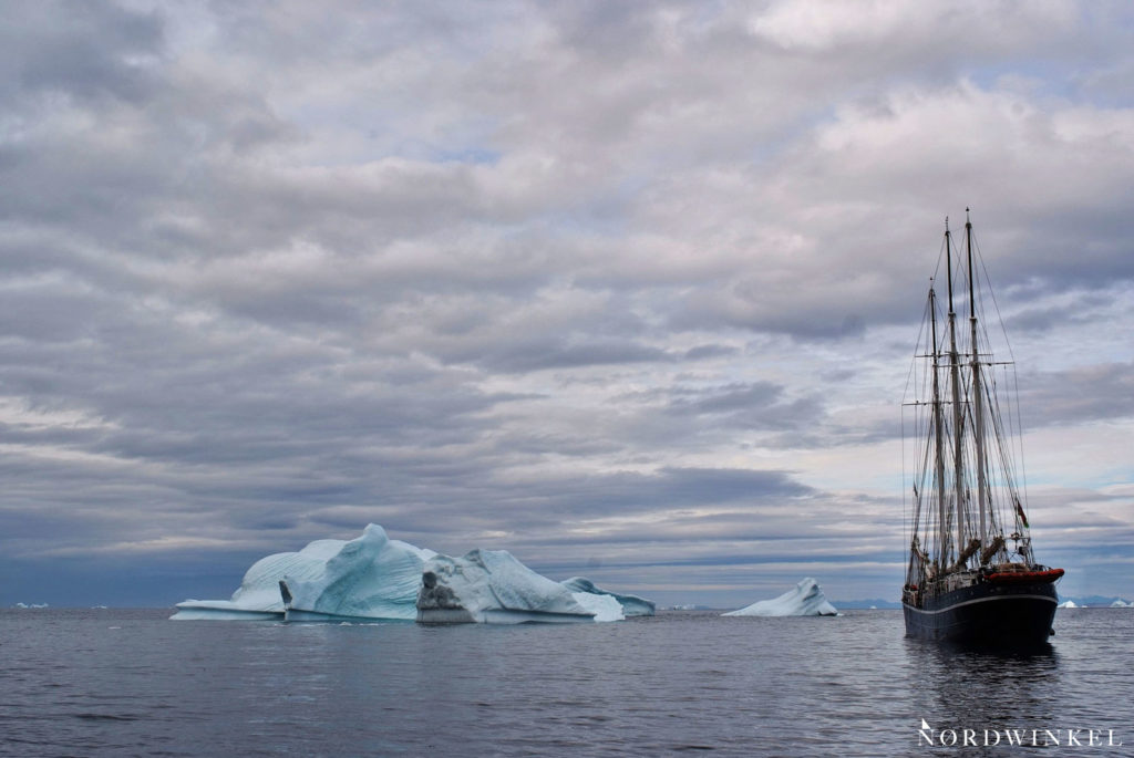 segelschiff zwischen blau leuchtenden eisbergen unter grauem himmel