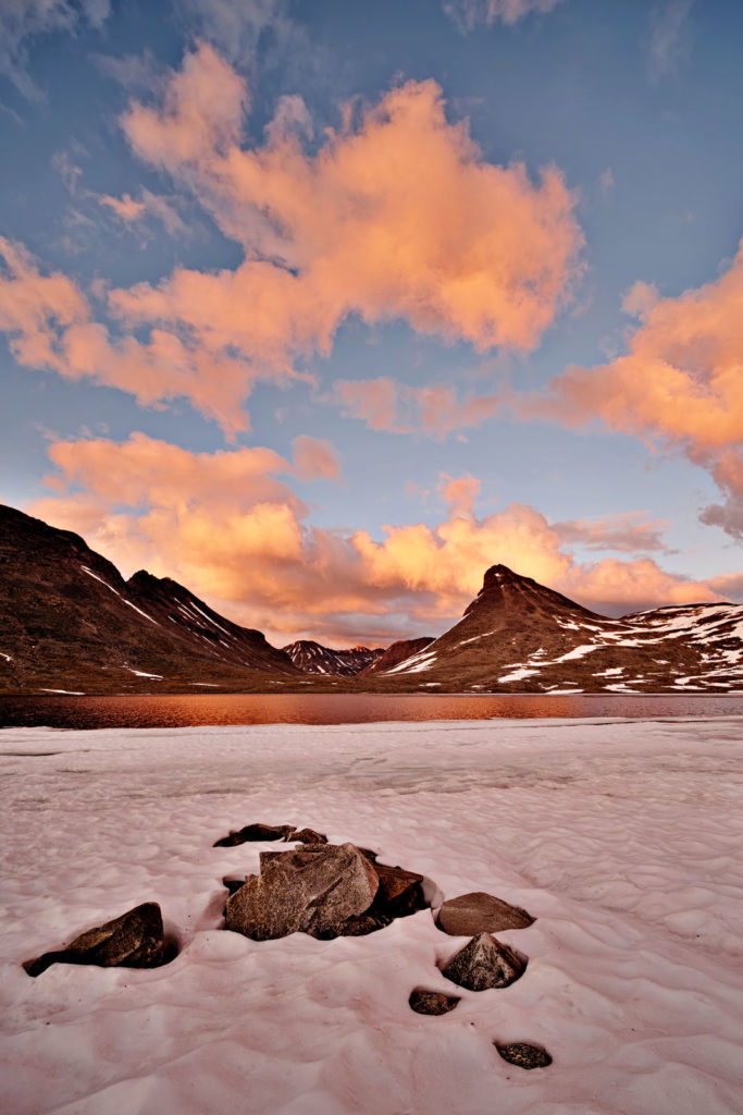 zugefrorener see im gebirge unter orangenen wolken